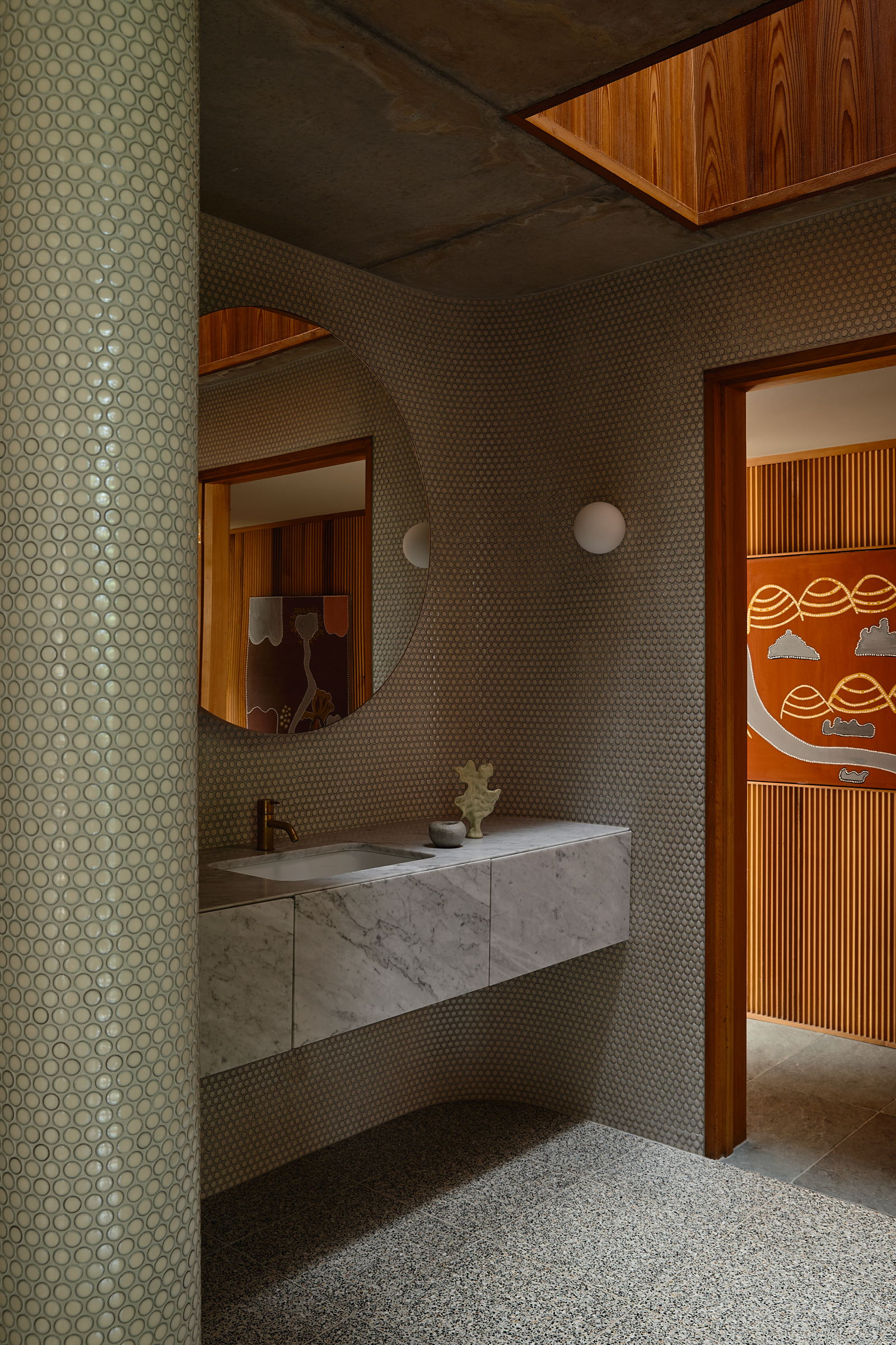 A bathroom sink with a large circular mirror, and a skylight