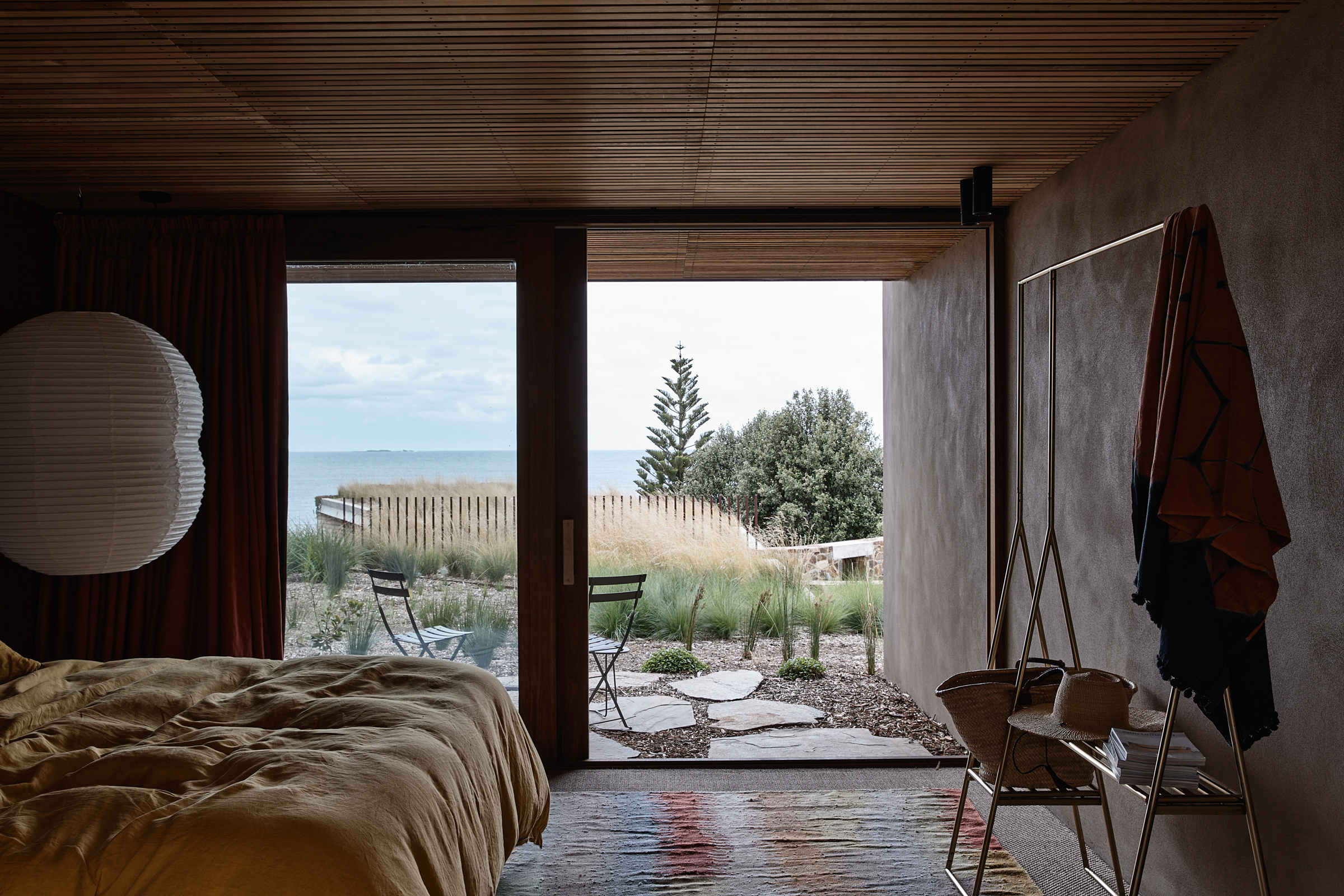 a bedroom with a timber slat ceiling, a rug and a view of the ocean.