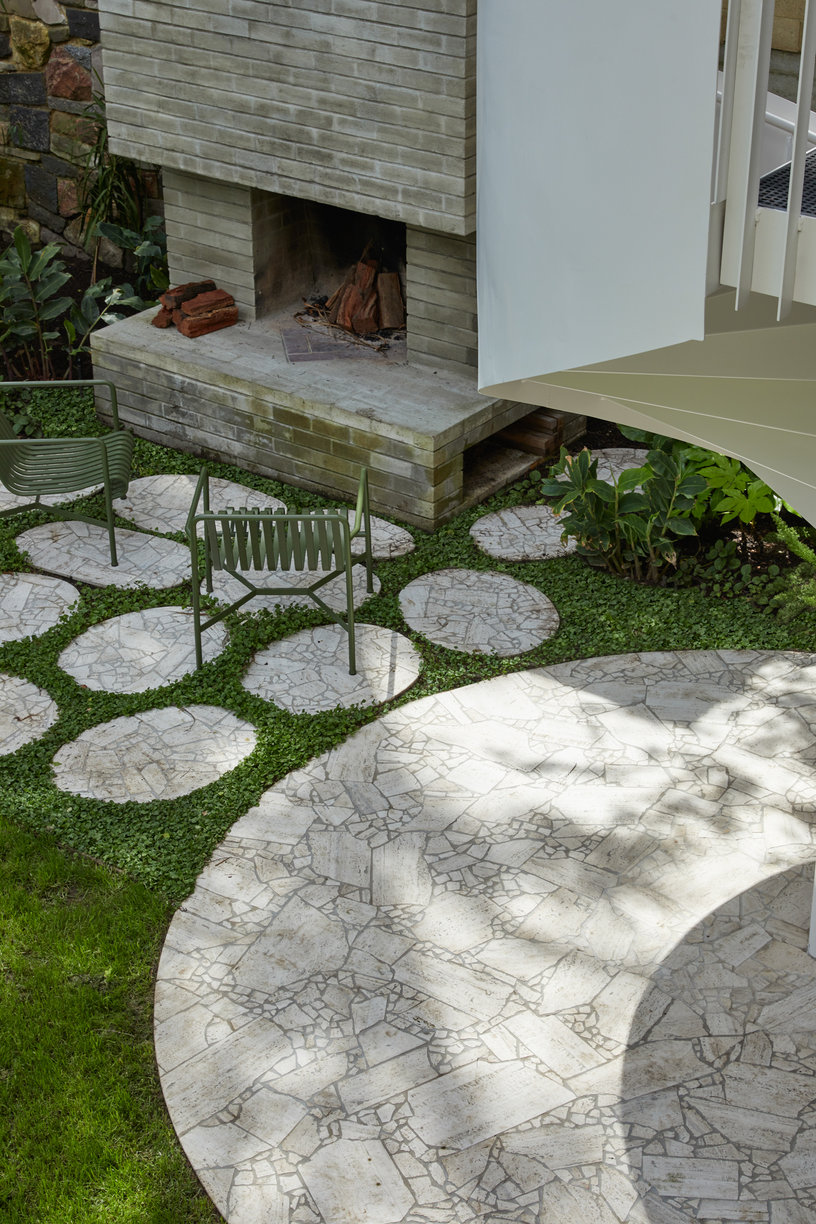 A backyard with grass, crazy paving and a fireplace.