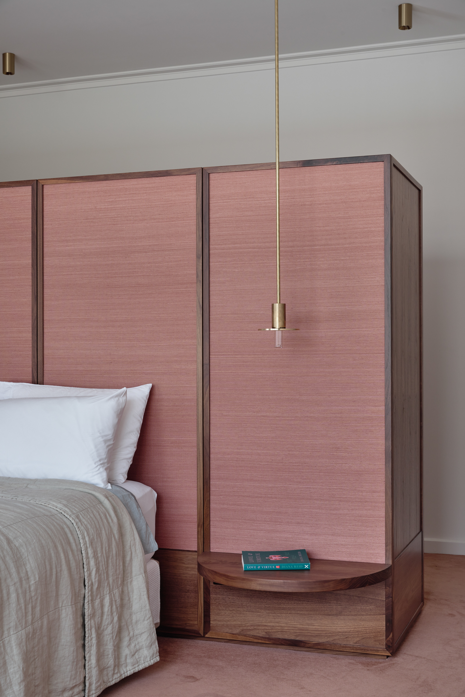 A bedroom with a pink dividing wall, pink carpet, a timber bedside table and a bed.