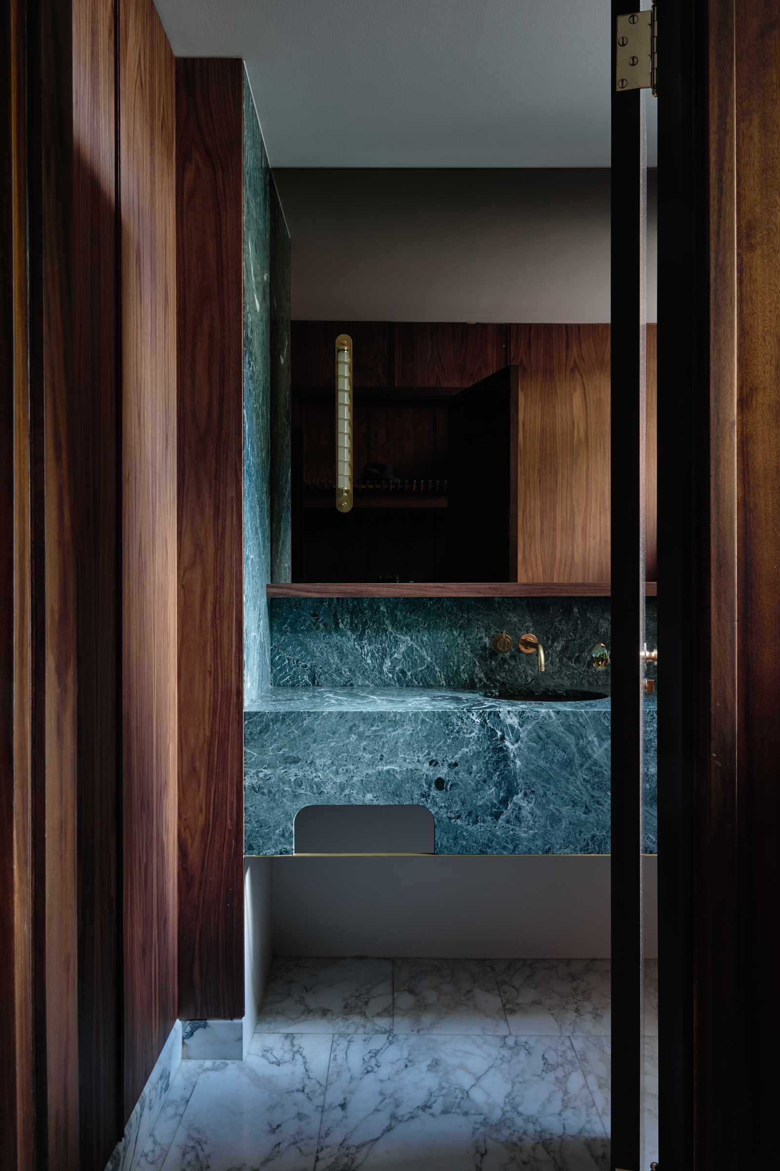 A bathroom with a green marble counter top, and dark timber shelving.