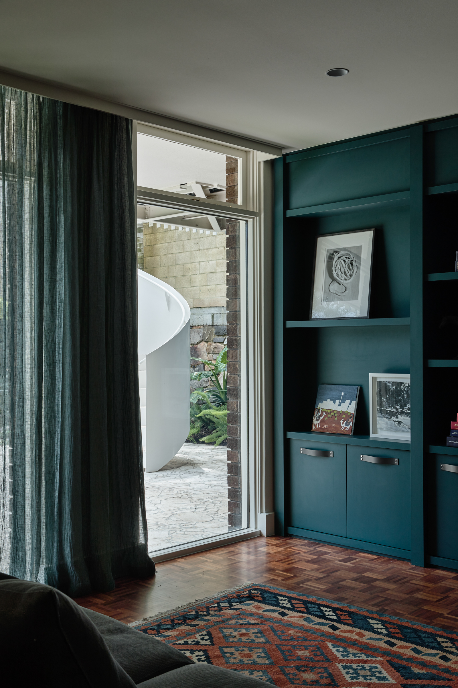 A living room with dark green walls and bookshelves, looking out onto a backyard.