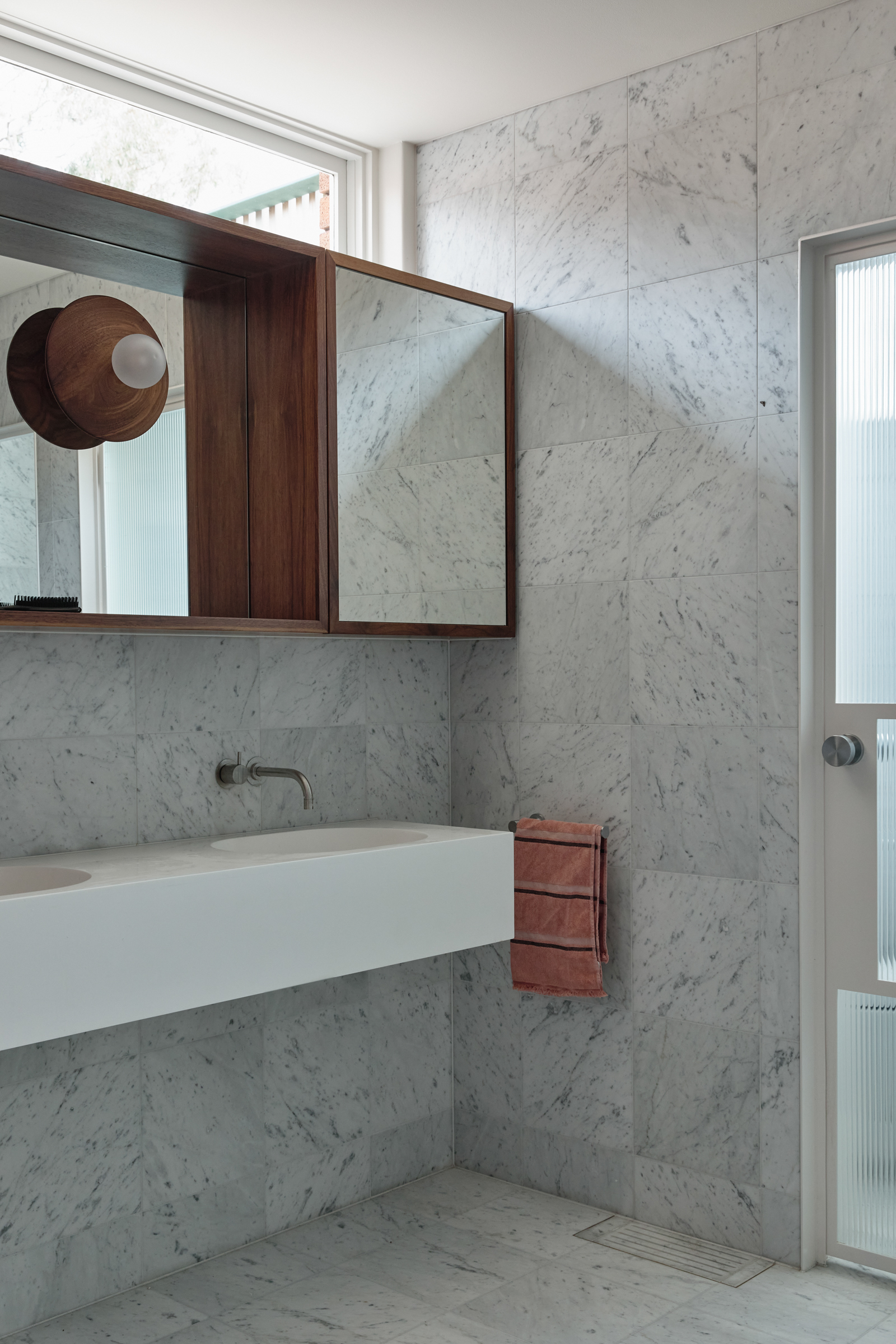 A bathroom with white marble walls, a mirror and a white sink.