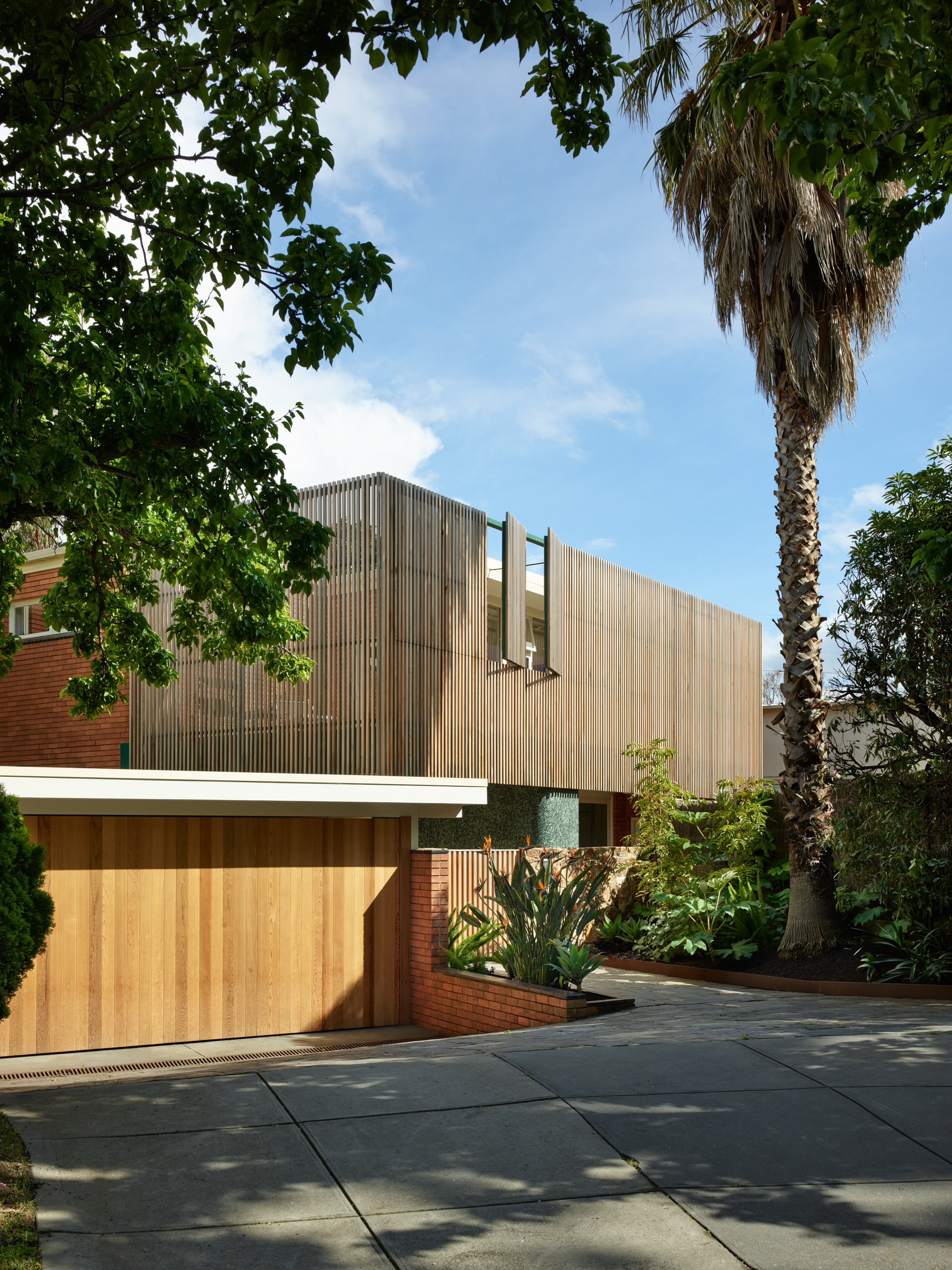 the facade of a modernist house with wooden slats and a driveway.