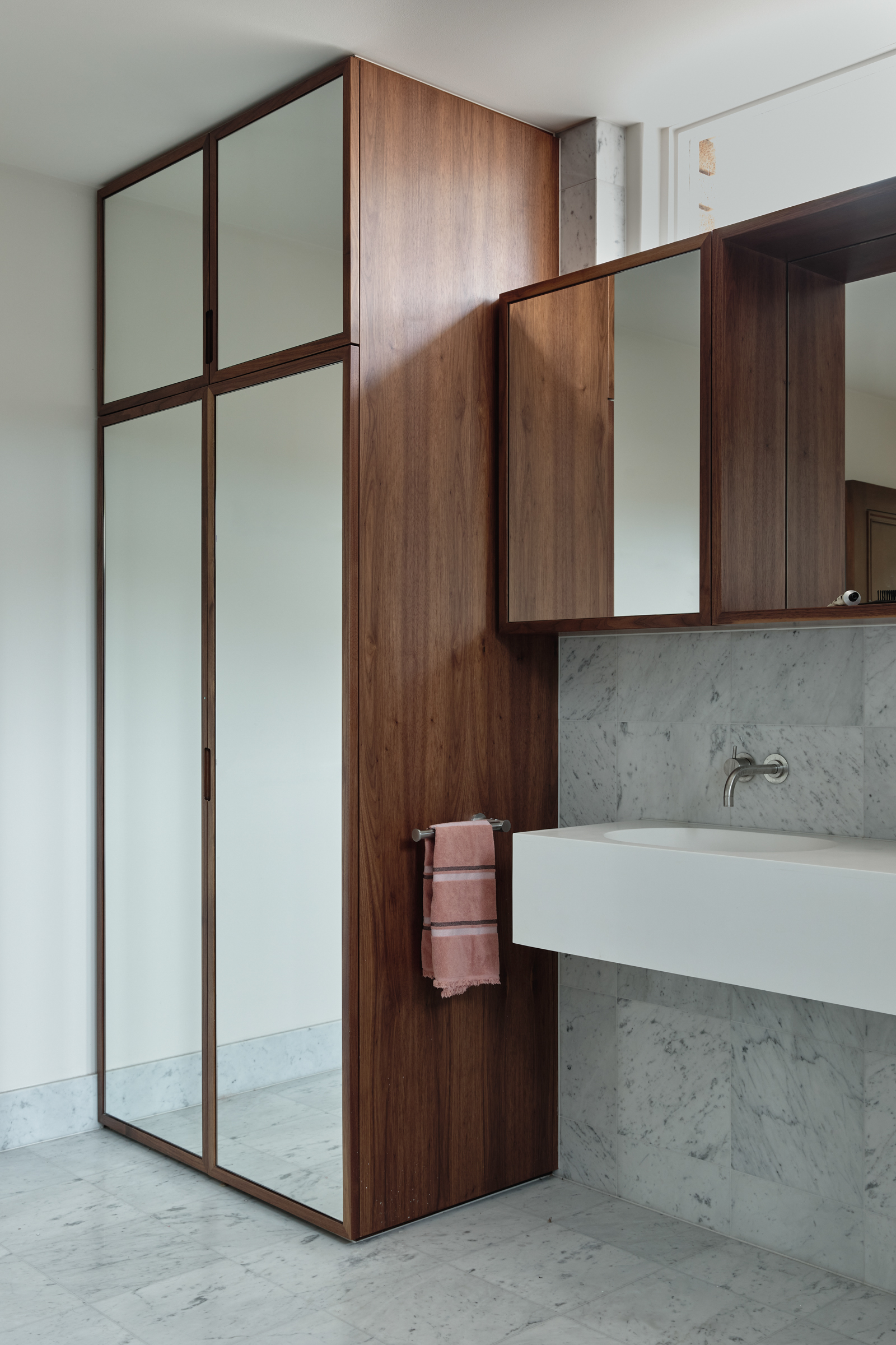 A bathroom with white marble walls, a mirror and timber clad cupboards.