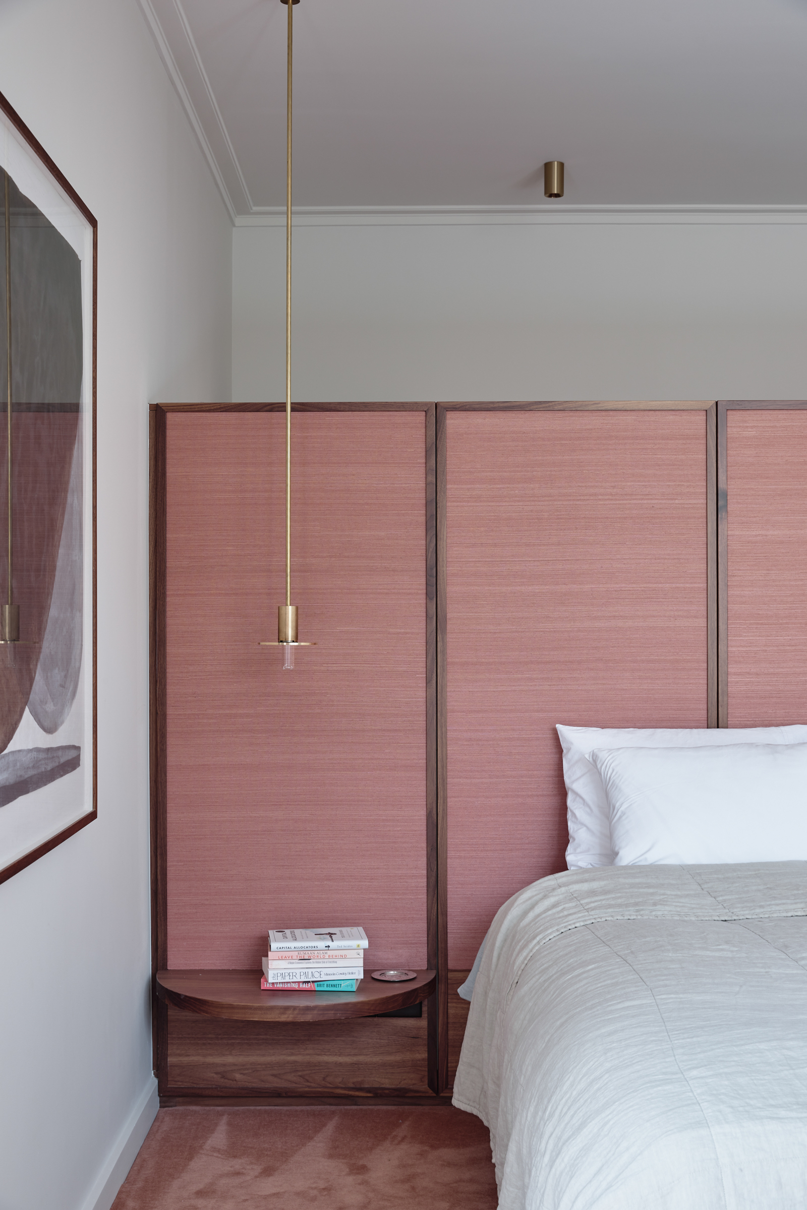 A bedroom with a pink dividing wall, pink carpet, a timber bedside table and a bed.