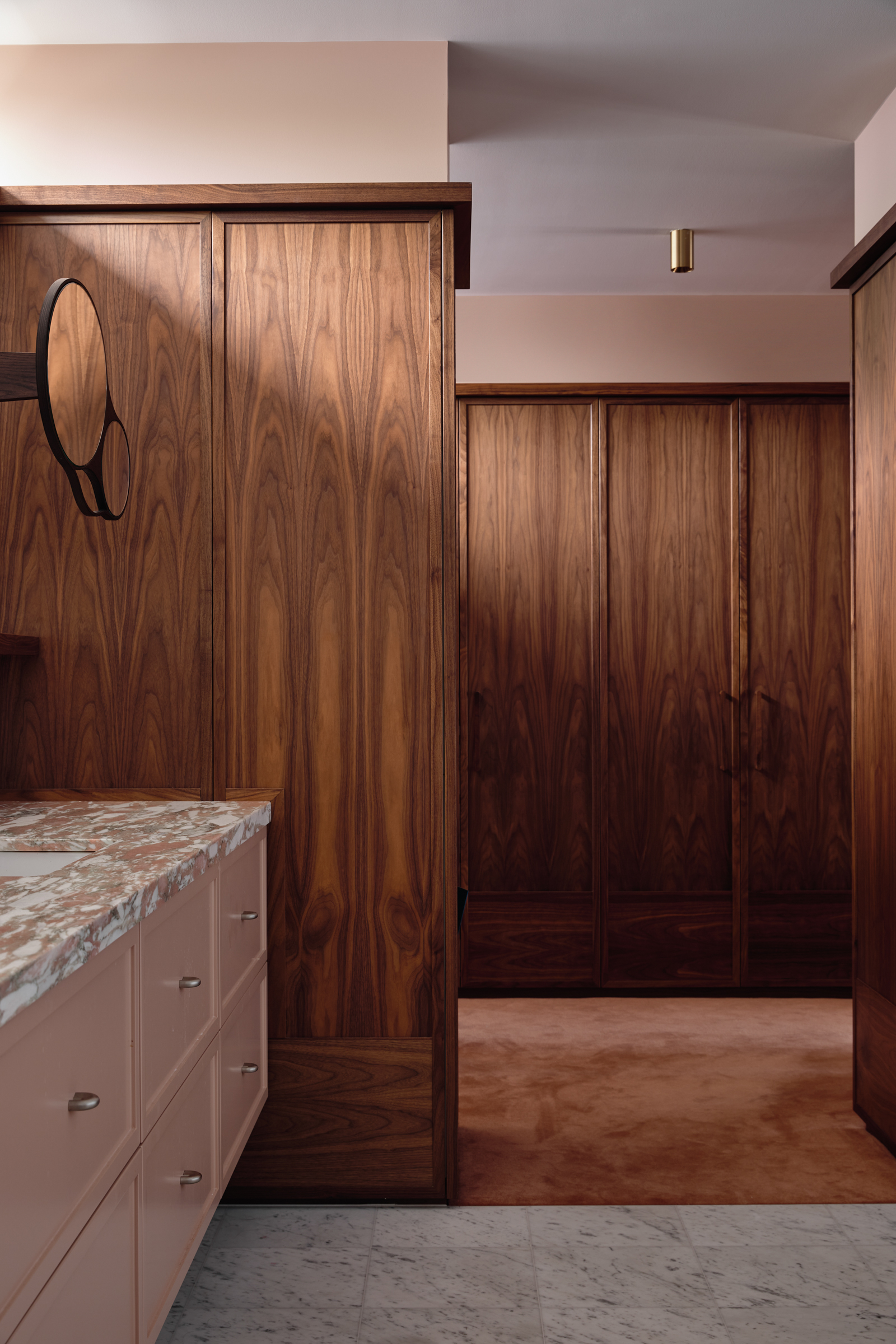 A bathroom with pink marble counter tops, leading onto a wooden panelled room.