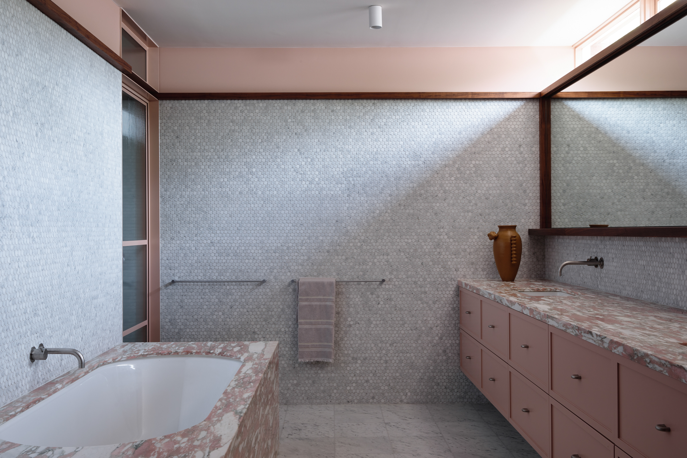 A bathroom with pink marble counter tops, and intricate white tiled walls.