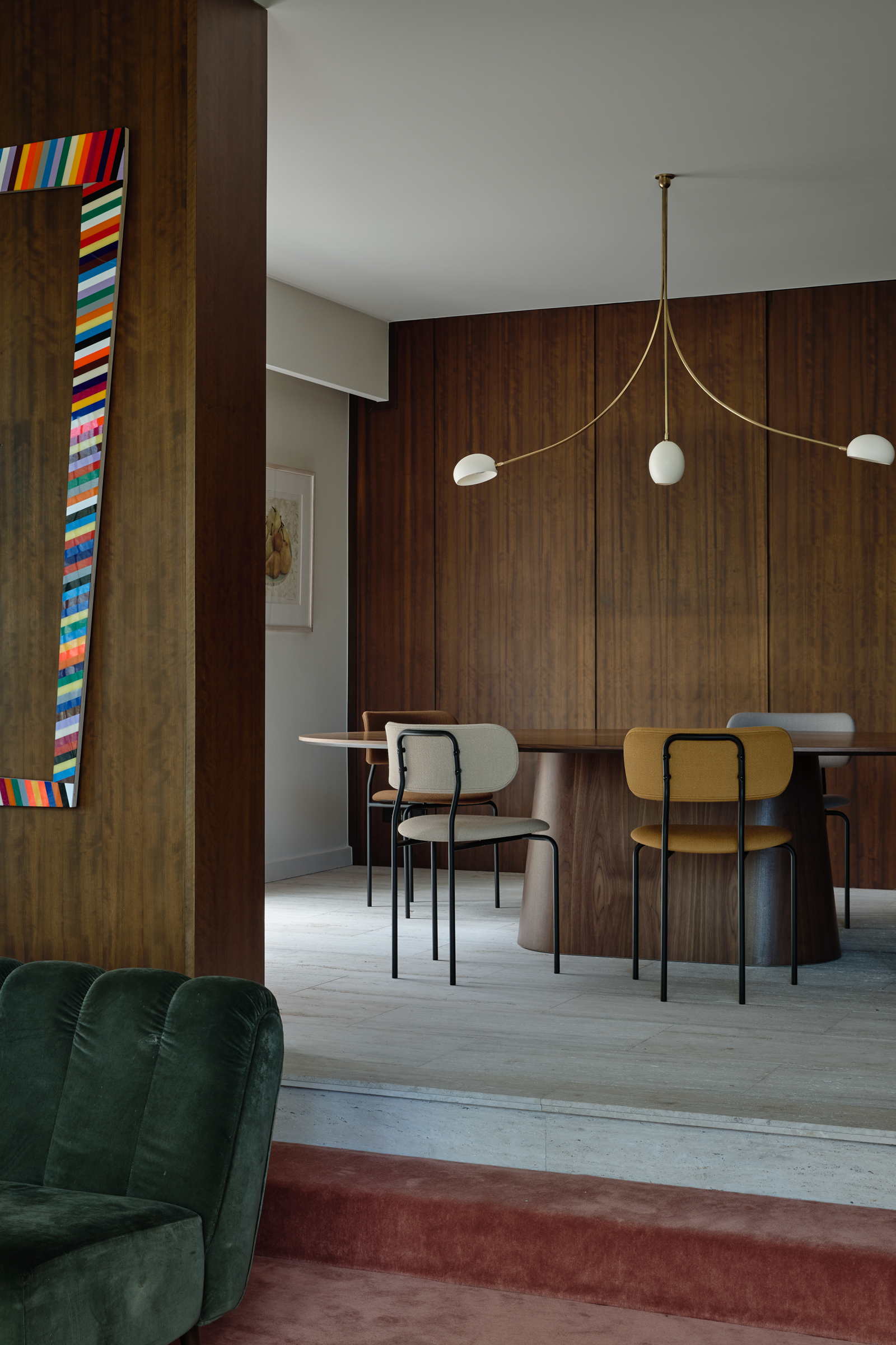 A sunken living room with a wooden panelled wall, looking onto the white marble floored dining room.