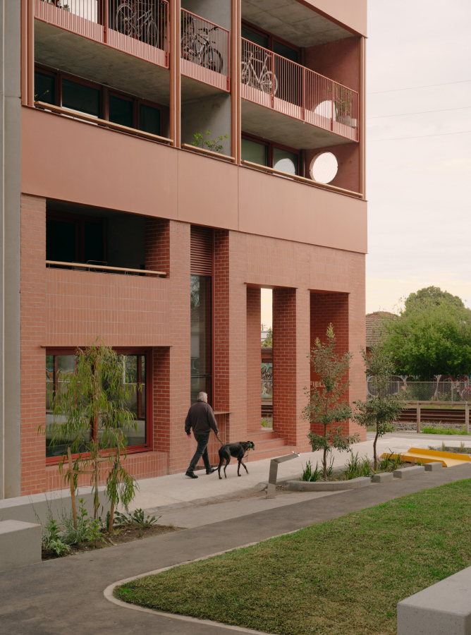 a man walking a dog on the street, infront of a red brick building.