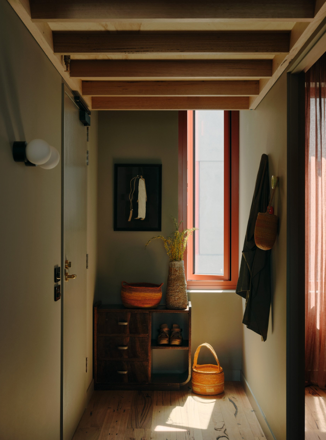 a hallway with a door, a window and a vase of flowers.