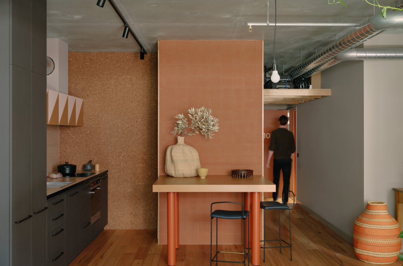 a man standing in a kitchen with a table and stools.
