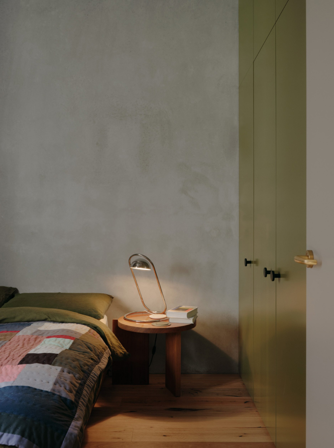 A bedroom with a bedside table, lamp and pale green cupboards.