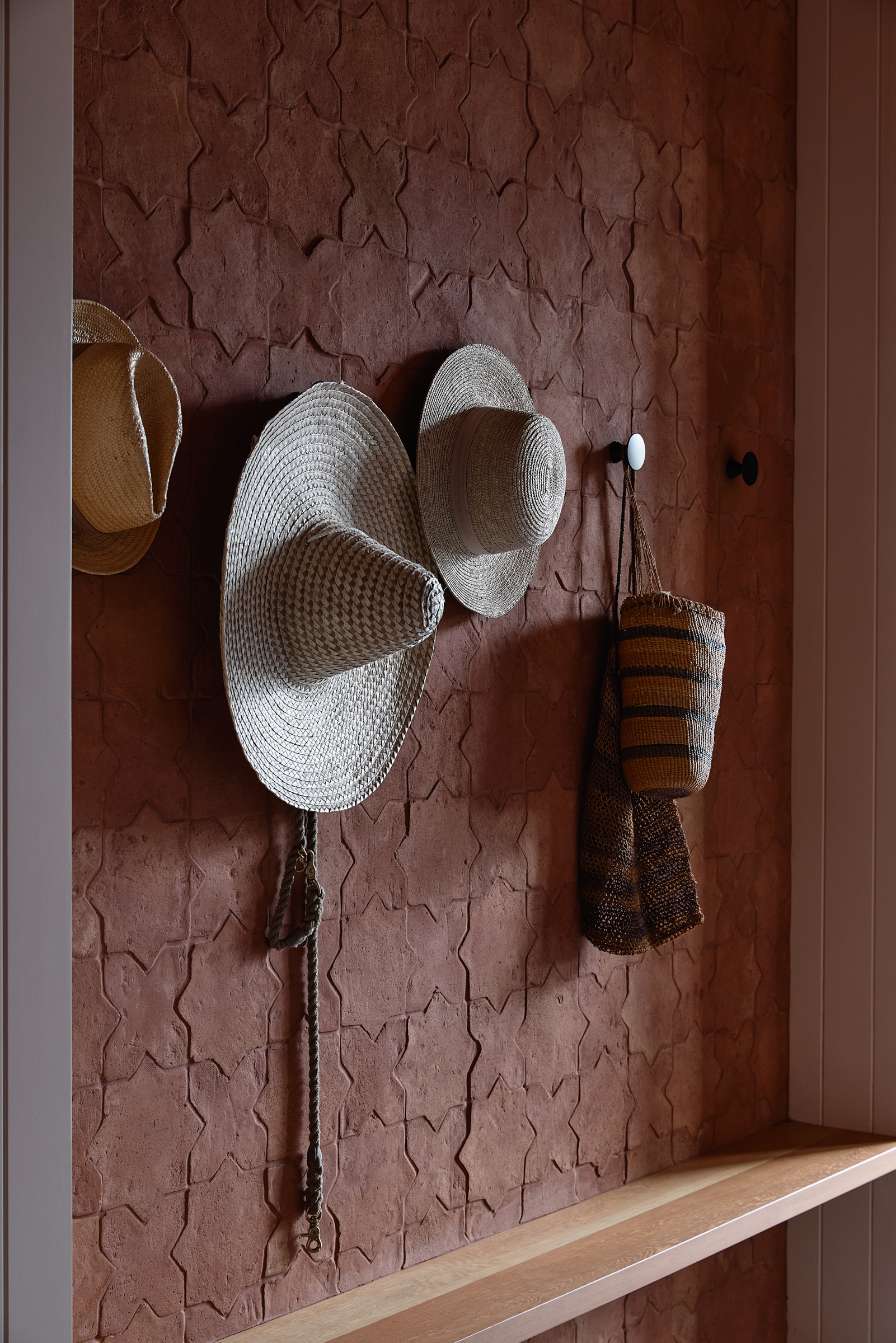 Three hats hanging on a wall, with a bench.