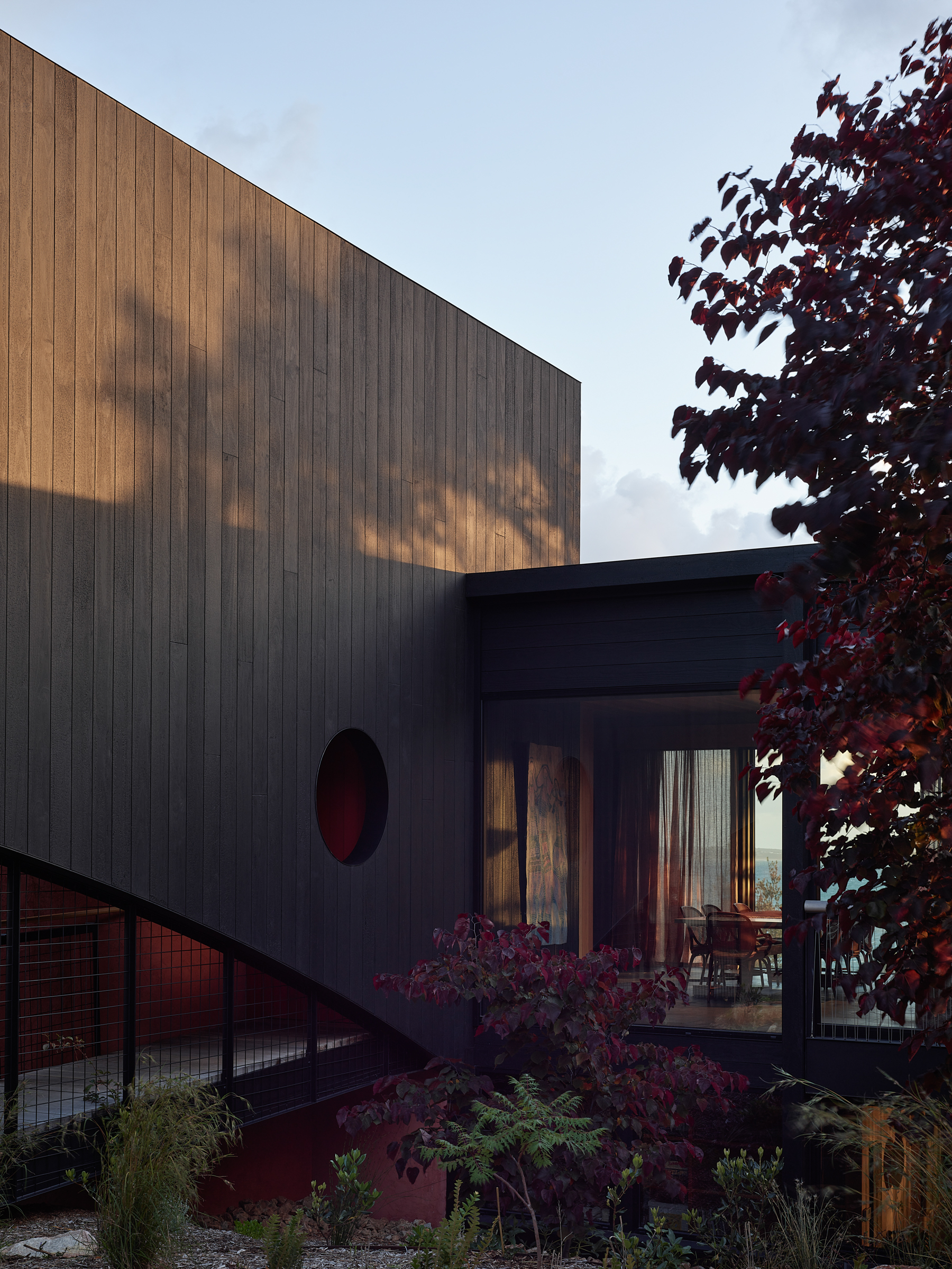 The exterior of a building with floor to ceiling glass windows, and a timber wall with a circular window.