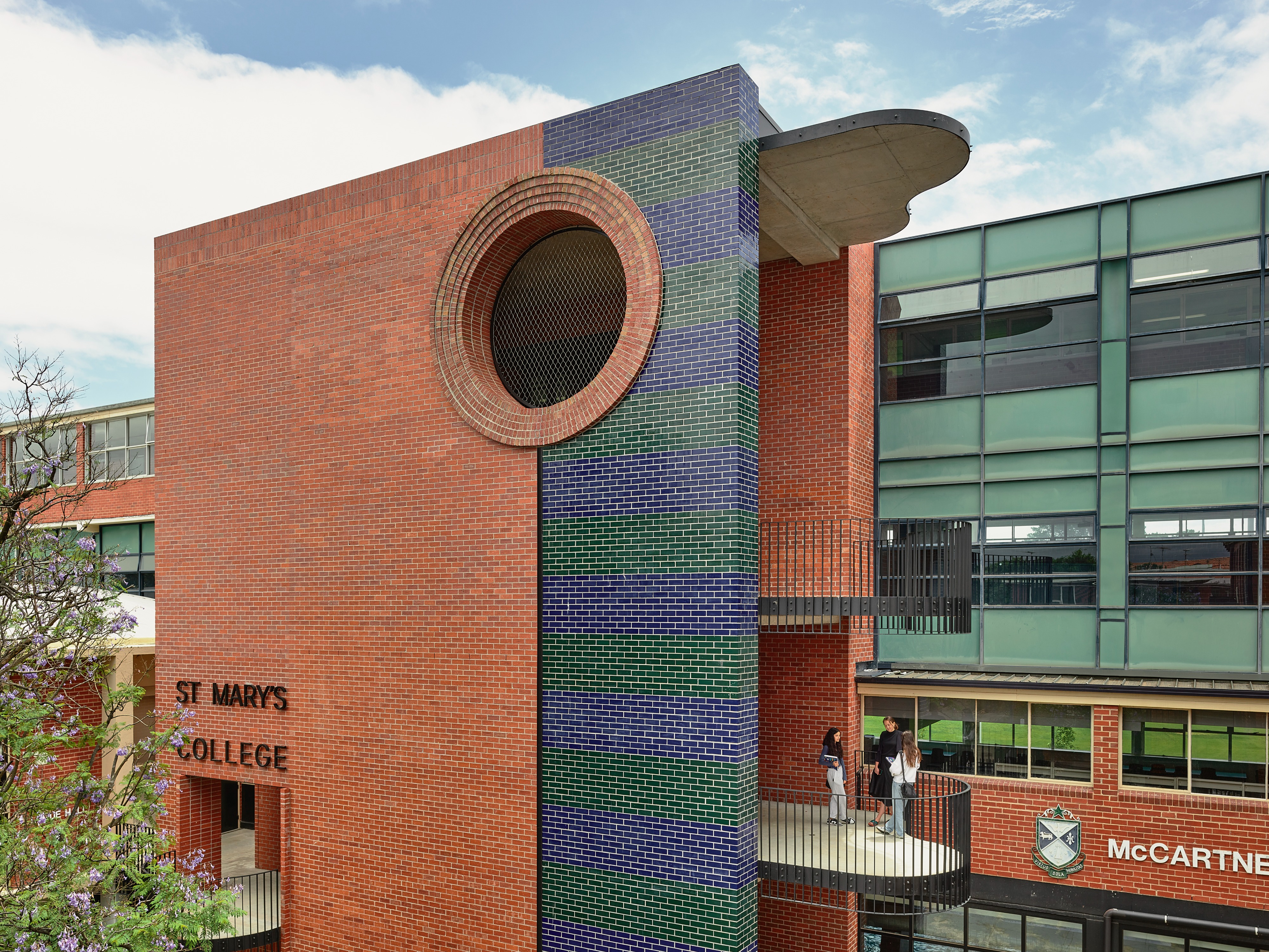 a red, blue and green brick building with a large circular window and staircase.