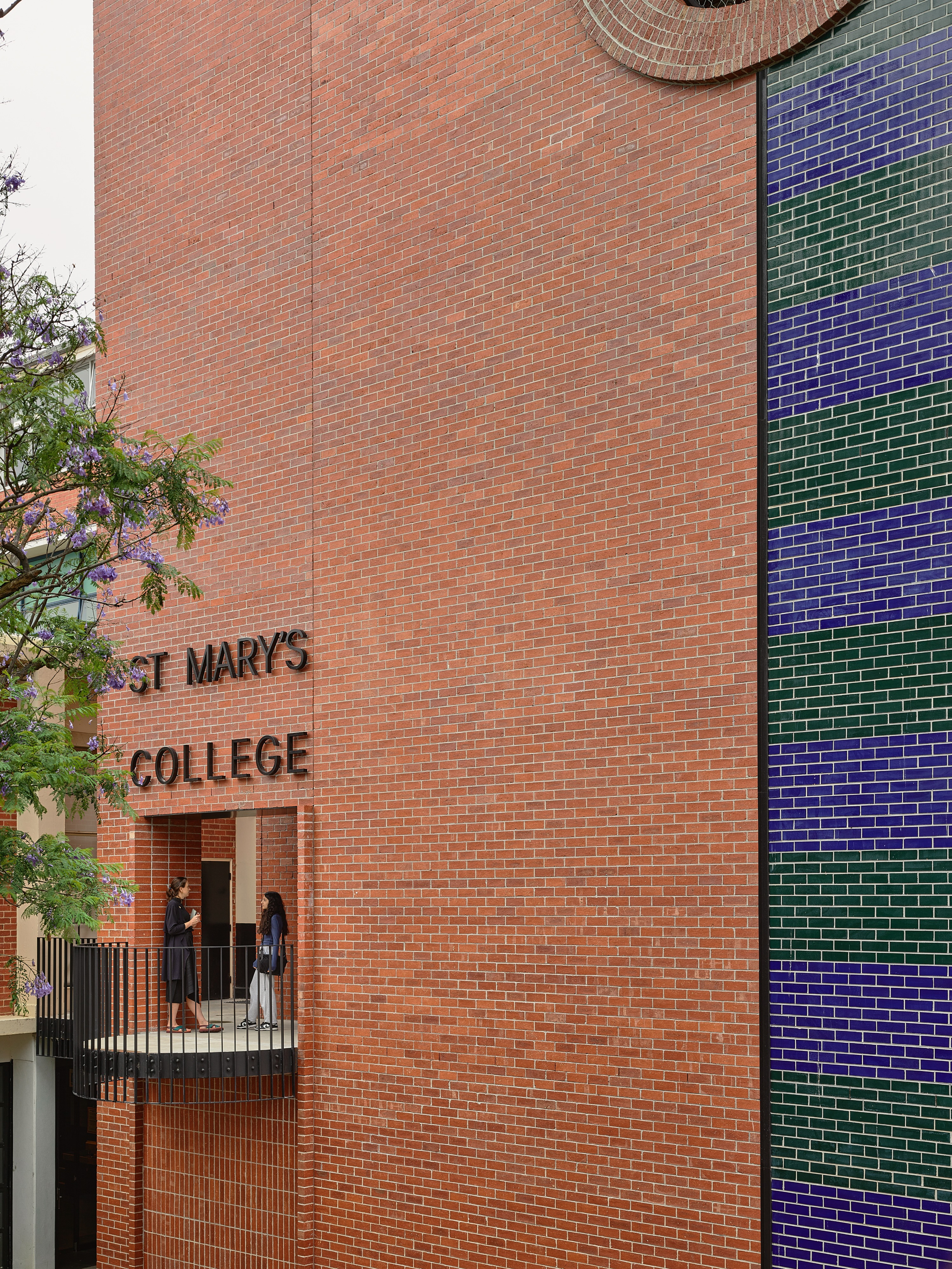 a red brick building with a balcony, and two people chatting.