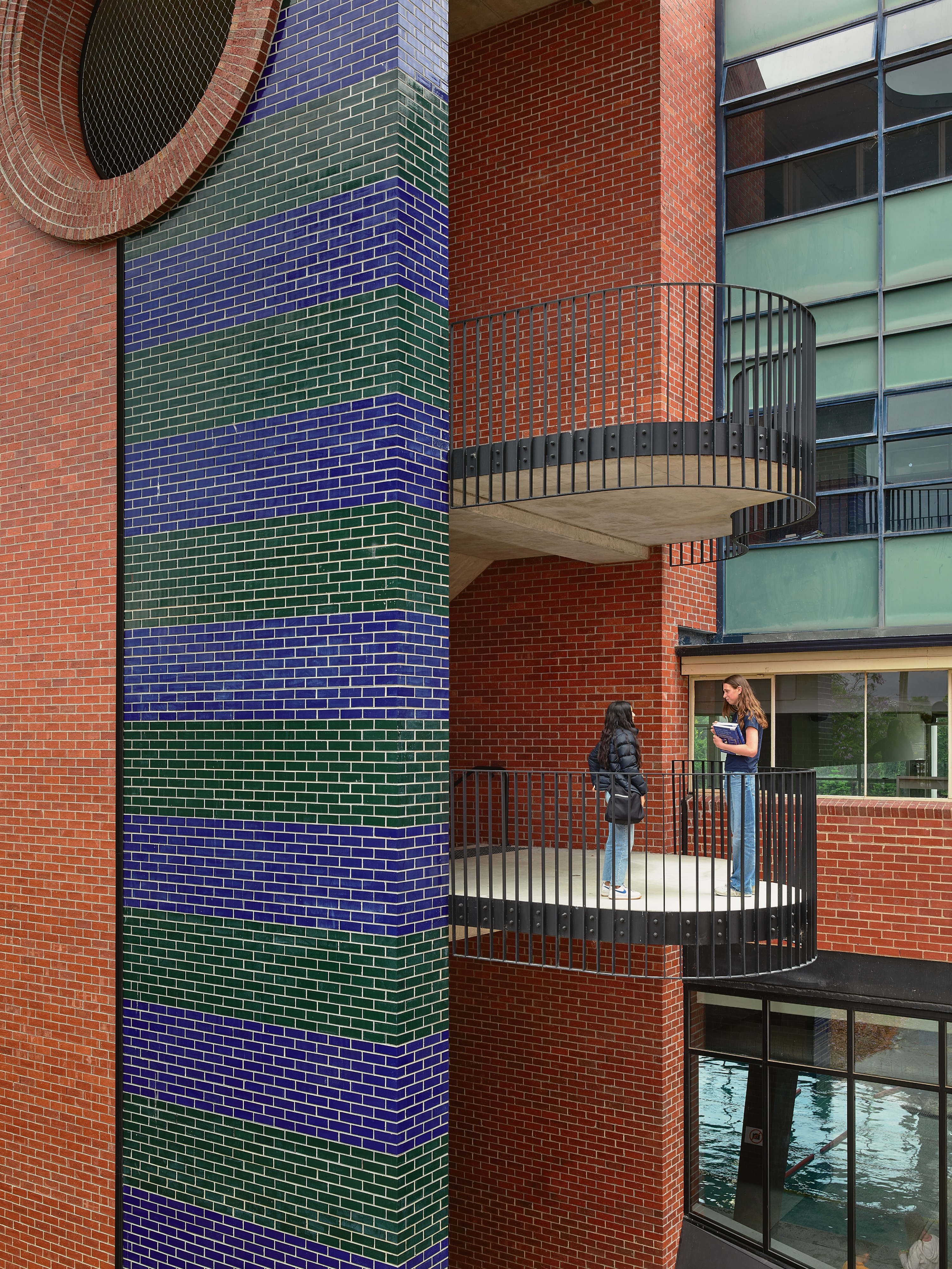 a red, blue and green brick building with a staircase, and two people chatting.