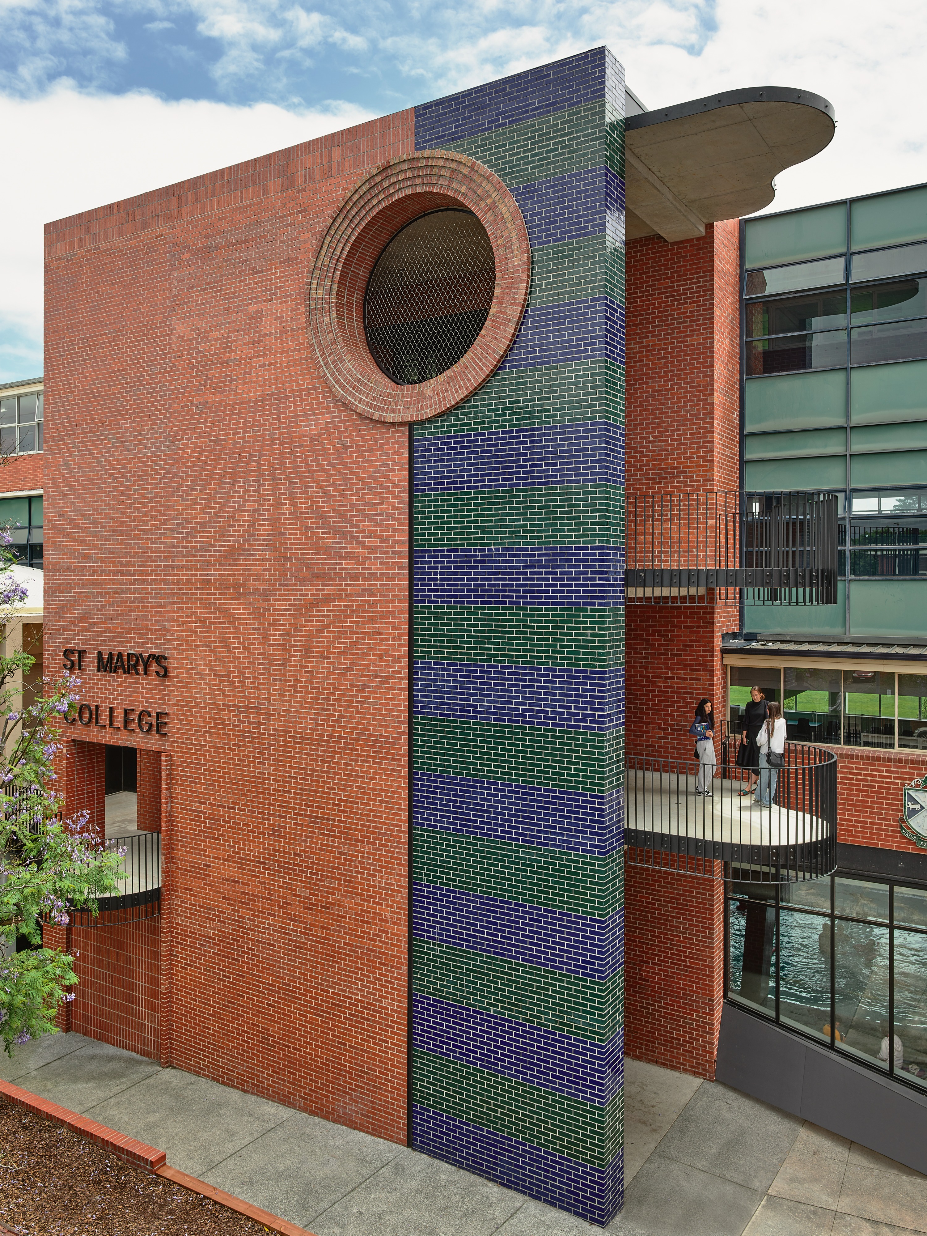 a red, blue and green brick building with a large circular window and staircase.