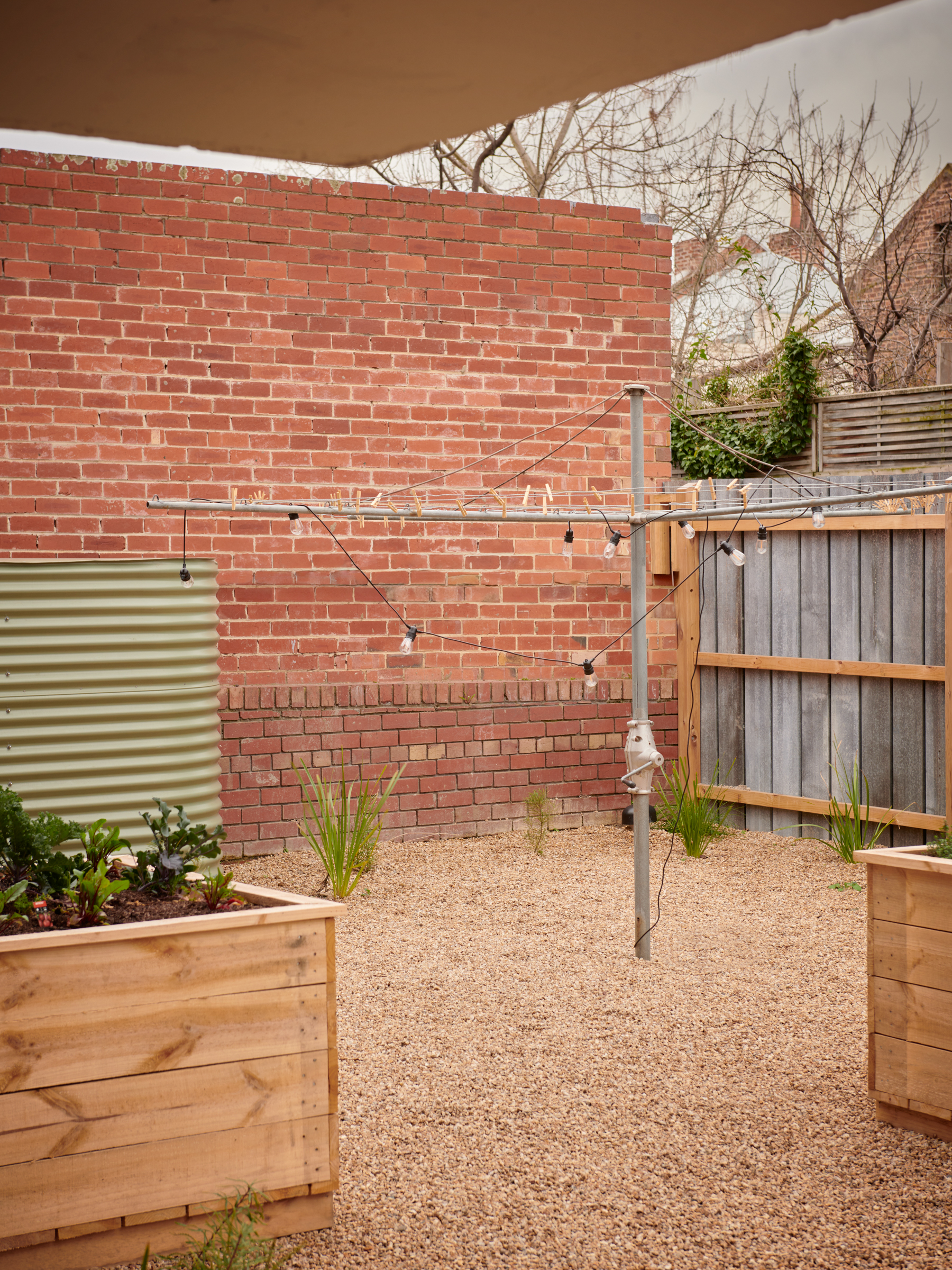 a brick wall in a gravel courtyard with raised planter boxes, and a hills hoist with lights.