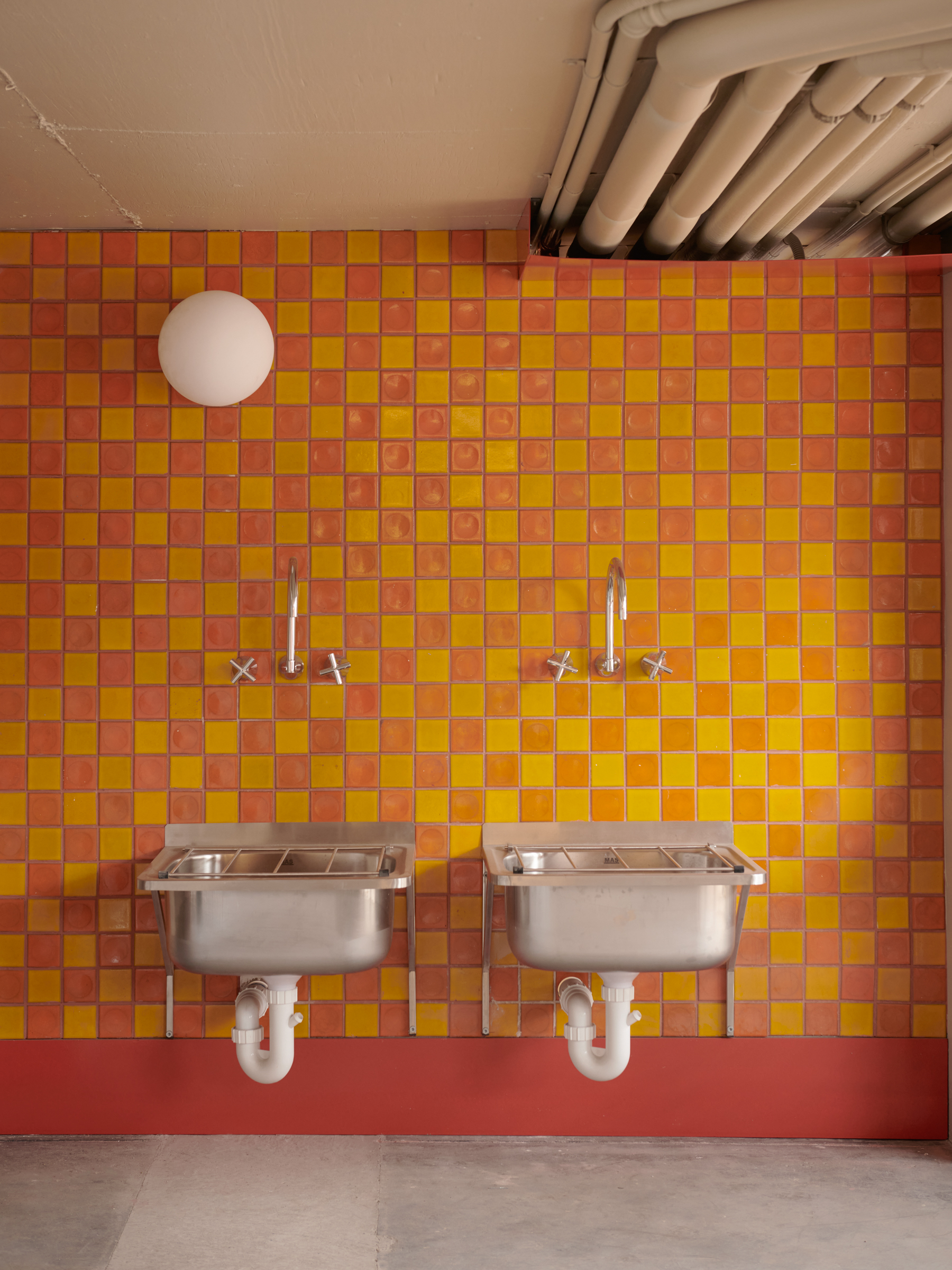 An orange and yellow checkerboard tiled wall with two laundry sinks.