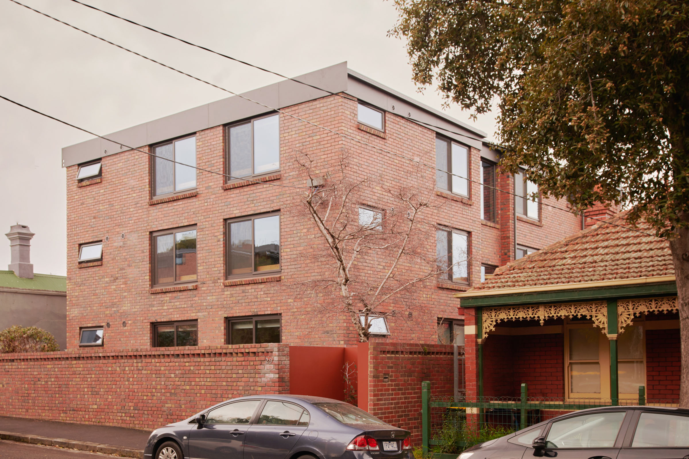 a three-storey, red brick building with cars parked in front of it.