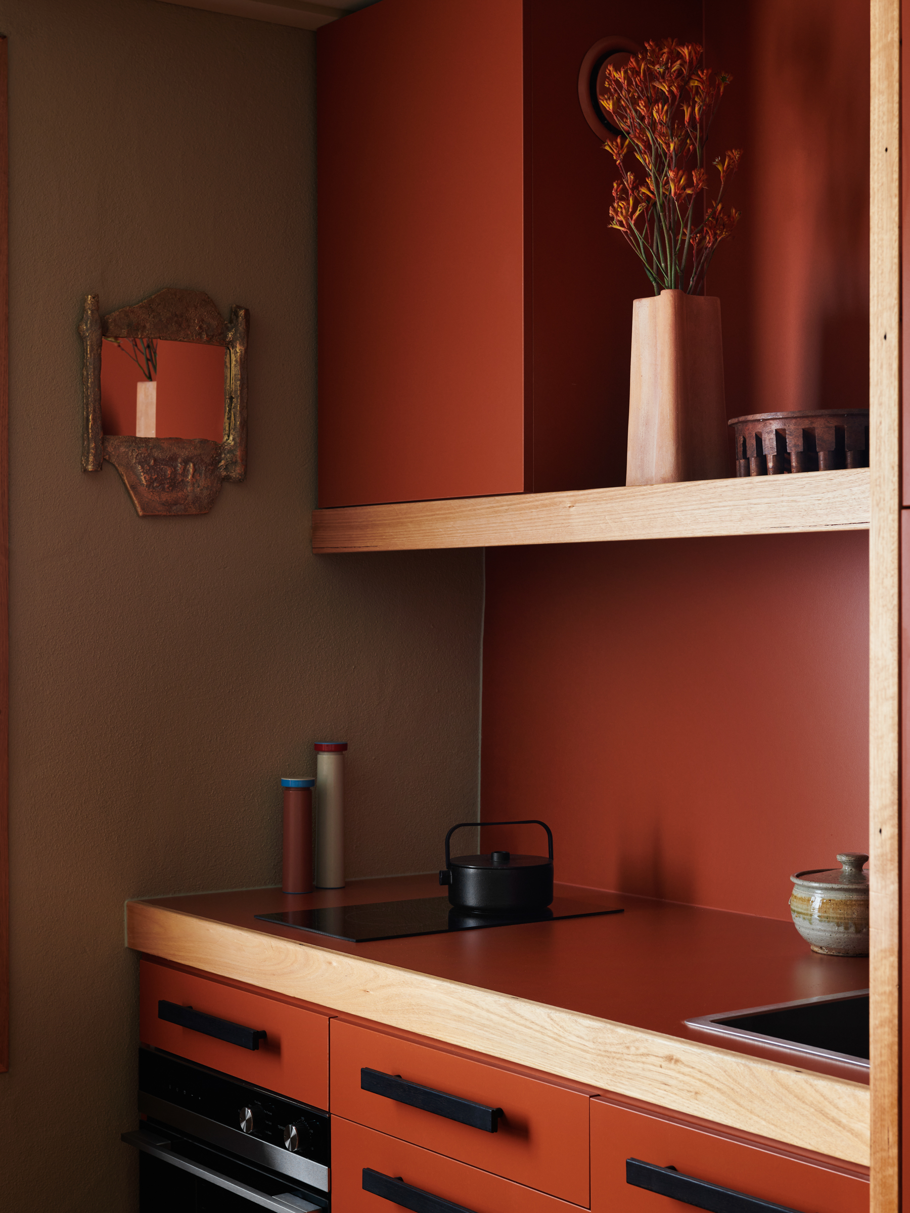 a deep red kitchen with a sink and shelf, and a mirror on the wall.