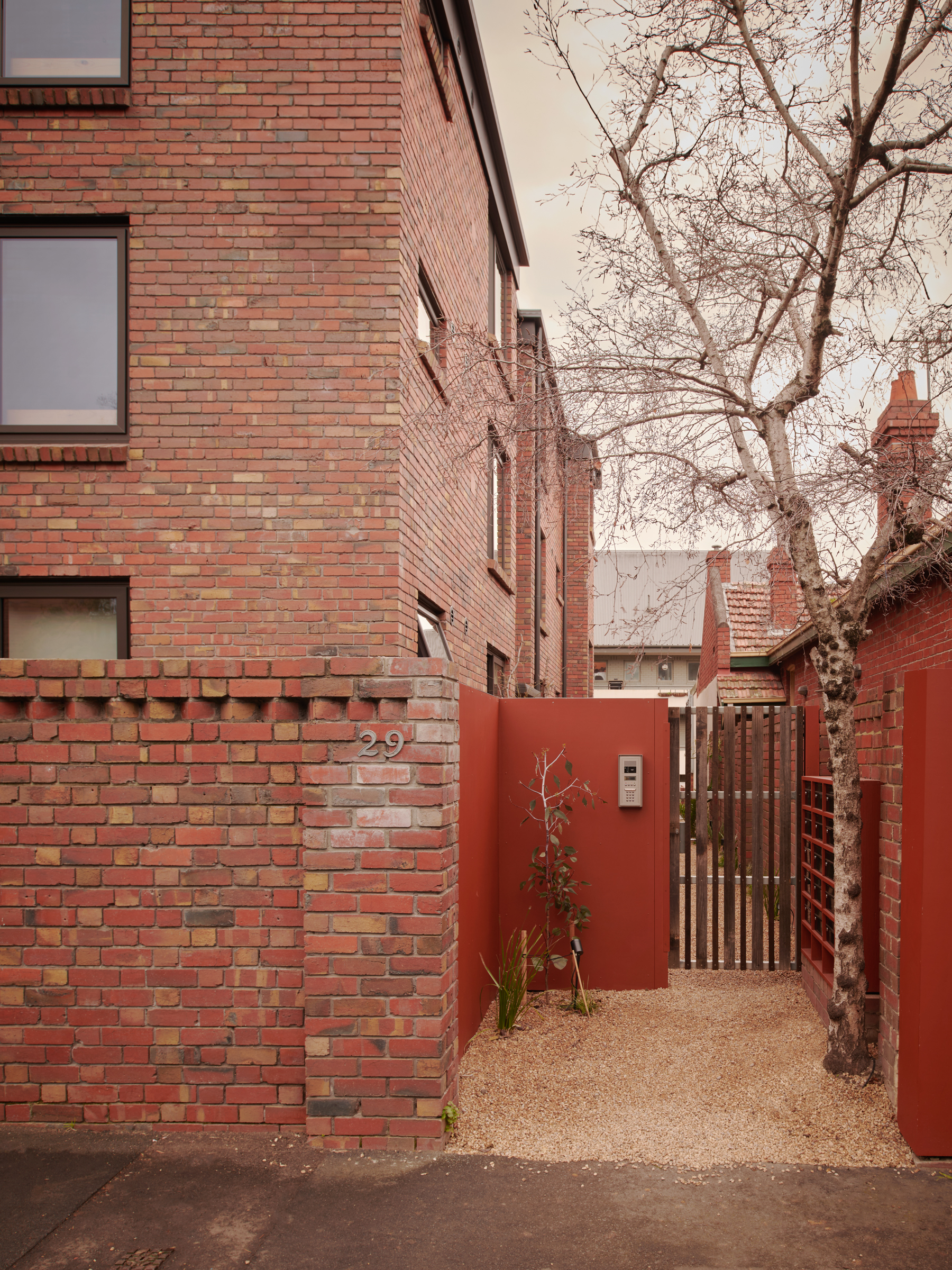 a brick building with a side entrance gate, with gravel paving and a tree